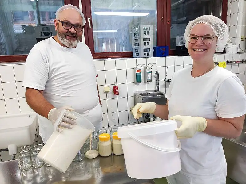 Bewohner und Werkstattmitarbeiter füllen gemeinsam Joghurt in Gläser ab.