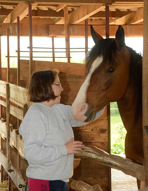Eine Bewohnerin lümmert sich liebevoll um ein Pferde des Hausenhofs