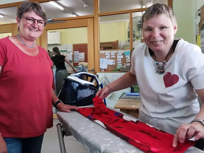 Mitarbeiterin und Bewohnerin arbeiten in der Wäscherei am Bügelbrett zusammen.