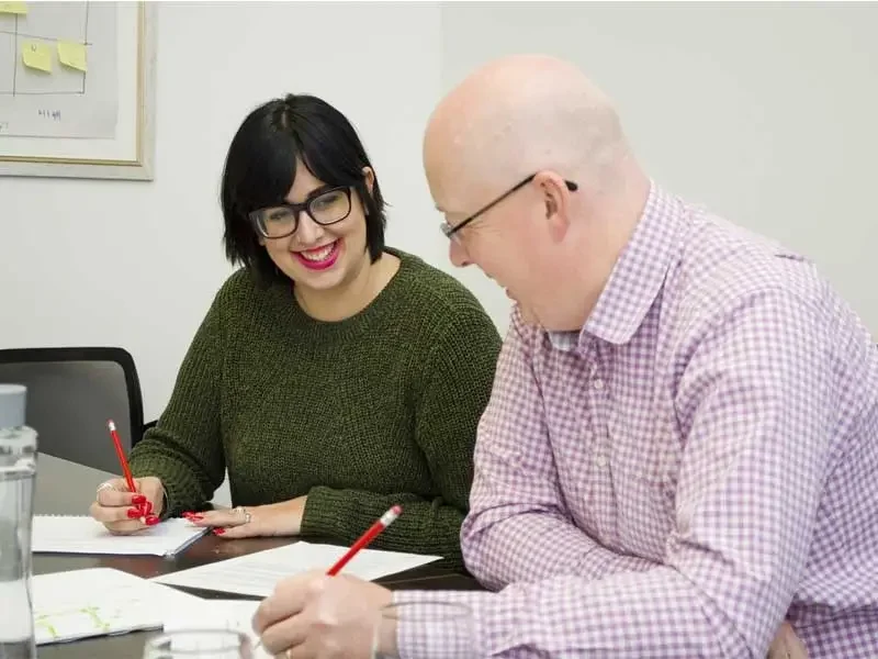 Zwei Kollegen sitzen am Schreibtisch und sprechen über das aktuelle Projekt des Auszubildenden